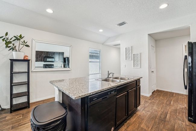 Kitchen with visible vents, dark wood finished floors, an island with sink, a sink, and black appliances | Image 7