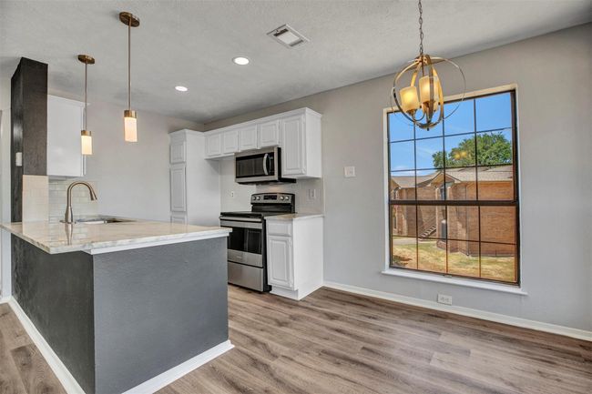 Kitchen with sink, tasteful backsplash, white cabinetry, kitchen peninsula, and stainless steel appliances | Image 6