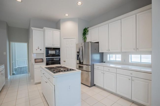 This kitchen is bright and spacious, featuring sleek white cabinetry, a central island with a cooktop. Ample counter space and large windows enhance the airy feel. | Image 20