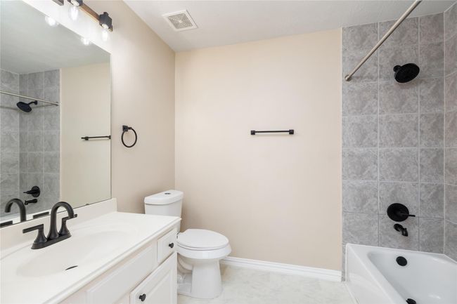 With modern features, this well-lit secondary bathroom includes a gray-tiled tub-shower combo, white vanity with black fixtures, and a large mirror. | Image 29