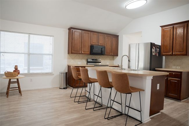 Kitchen featuring stainless steel appliances, a sink, a breakfast bar, a kitchen island with sink, and light countertops | Image 6