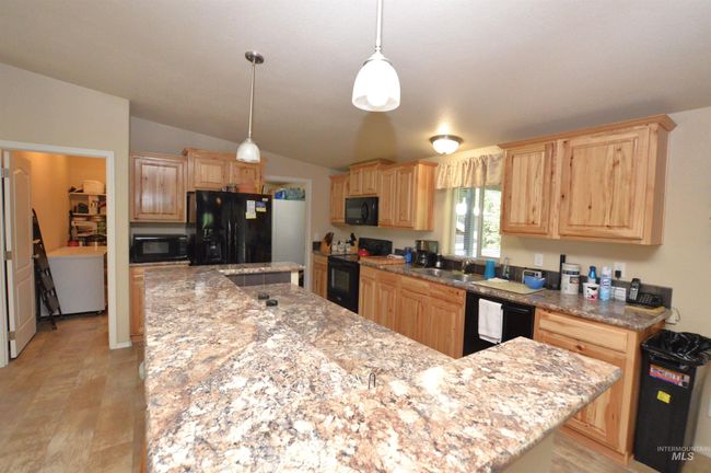 Kitchen with black appliances, a center island, light brown cabinetry, light stone countertops, and pendant lighting | Image 8