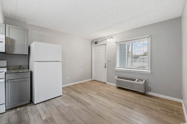 Kitchen with white appliances, light wood-style flooring, a textured ceiling, gray cabinetry, and a wall mounted AC | Image 7