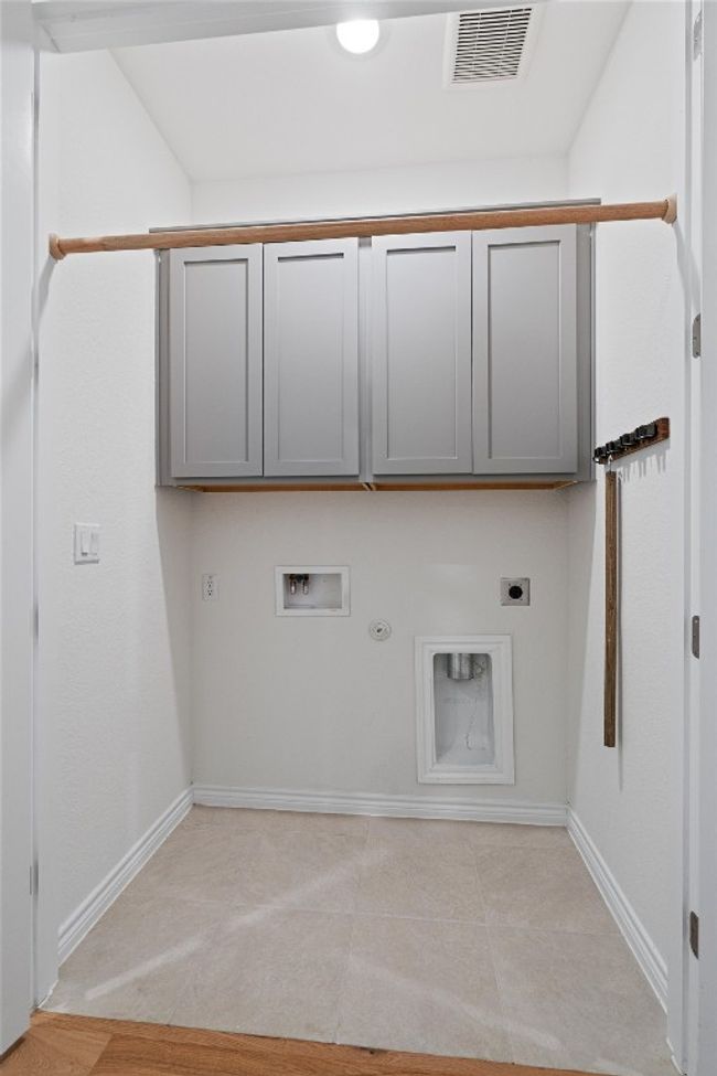 Clothes washing area featuring tile flooring and wood cabinets for storage. | Image 21