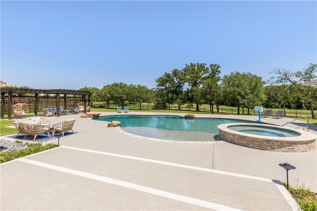 View of pool featuring a pergola, a patio, a pool with connected hot tub, a lawn, and an outdoor hangout area | Image 17