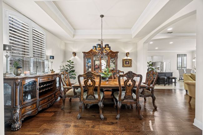 Dining area featuring a chandelier, crown molding, a tray ceiling, arched walkways, and dark wood floors | Image 4