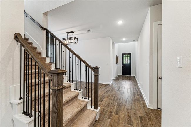 As you enter the home through the bright entryway with high ceilings and a modern light fixture, your attention is drawn to the open staircase with sleek railings & iron balusters, leading to the upper level. | Image 5