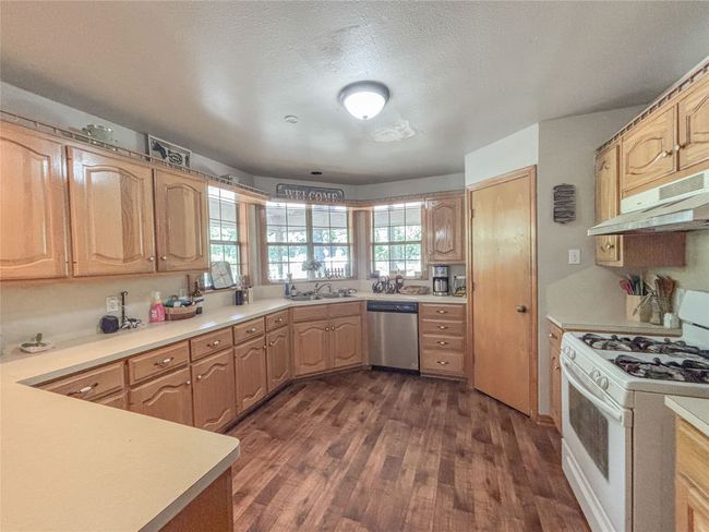 Kitchen with dark wood finished floors, under cabinet range hood, white gas range, dishwasher, and a sink | Image 7
