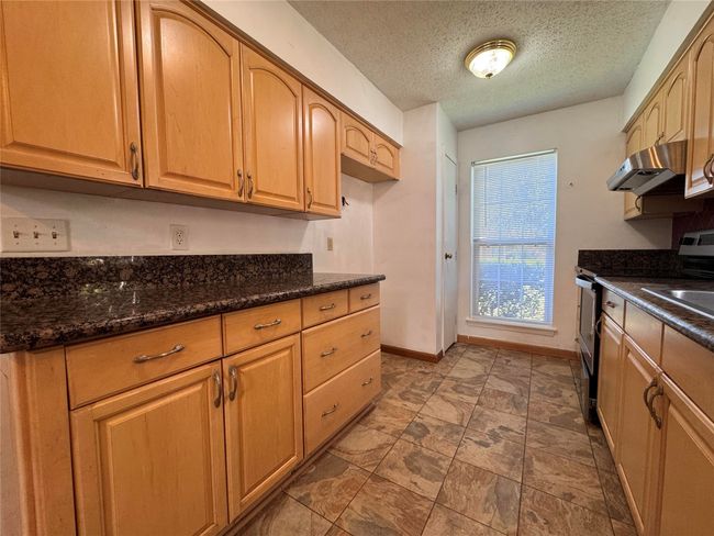 Kitchen with under cabinet range hood, stainless steel stove, a textured ceiling, and dark stone countertops | Image 5