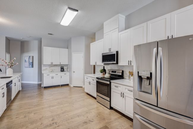 Kitchen with stainless steel appliances, light countertops, white cabinets, light wood-style flooring, and tasteful backsplash | Image 10