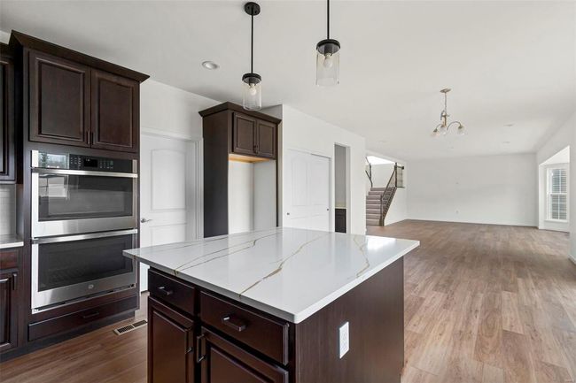 Kitchen featuring dark brown cabinetry, a center island, stainless steel double oven, decorative light fixtures, and light wood-type flooring | Image 20