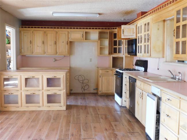 Kitchen featuring a textured ceiling, sink, white appliances, and light wood-type flooring | Image 6