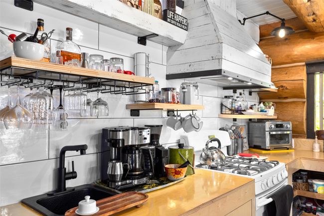 Kitchen featuring open shelves, gas range gas stove, wall chimney range hood, backsplash, and beamed ceiling | Image 6