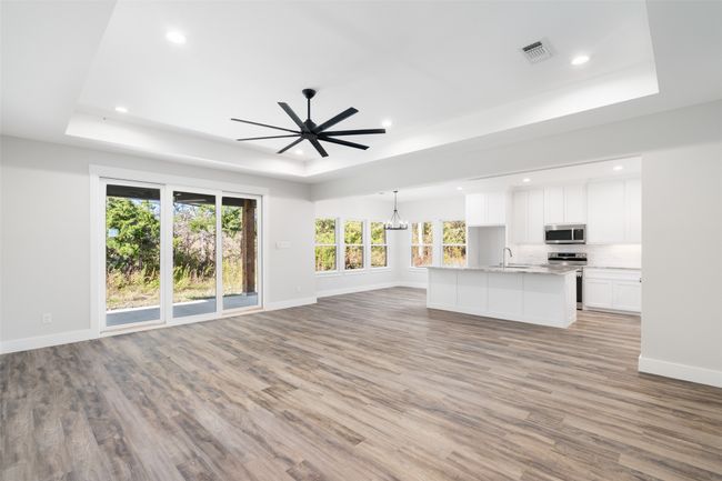 Unfurnished living room featuring ceiling fan with notable chandelier, a raised ceiling, sink, and light hardwood / wood-style flooring | Image 10