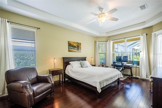 Spacious Primary Room with rich wood flooring, a private door entry to lanai, and large windows revealing the lush green natural park behind the home. | Image 19