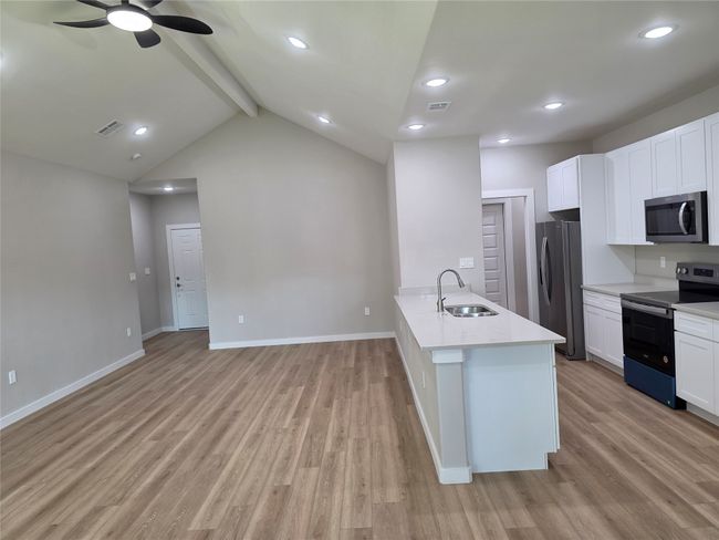 Kitchen with stainless steel appliances, a sink, light wood-type flooring, ceiling fan, and baseboards with living area. | Image 4