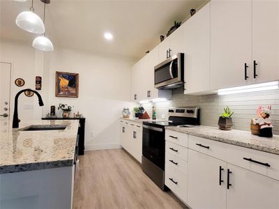 Kitchen with backsplash, appliances with stainless steel finishes, sink, light wood-type flooring, and white cabinets | Image 3