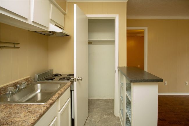 Kitchen featuring electric stove, crown molding, white cabinetry, under cabinet range hood, and wooden walls | Image 4