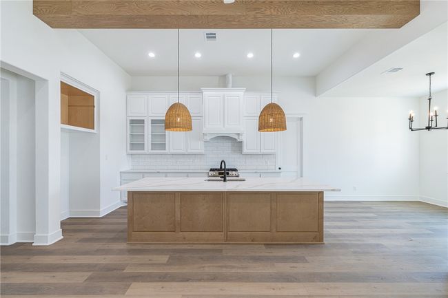 Kitchen with a large island, hardwood / wood-style floors, hanging light fixtures, white cabinetry, and light stone counters | Image 9