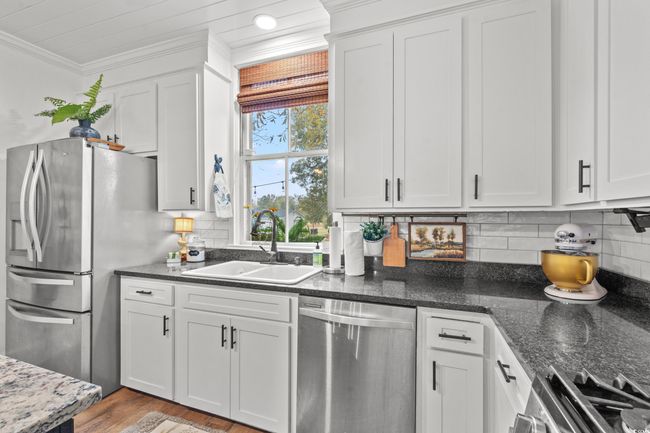 Kitchen featuring stainless steel appliances, ornamental molding, white cabinetry, tasteful backsplash, and dark stone counters | Image 8