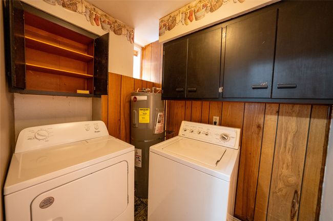 Washroom featuring cabinet space, independent washer and dryer, water heater, and wood walls | Image 23