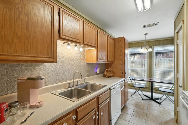 Kitchen with dishwasher, light countertops, decorative light fixtures, light tile patterned floors, and brown cabinetry | Image 8