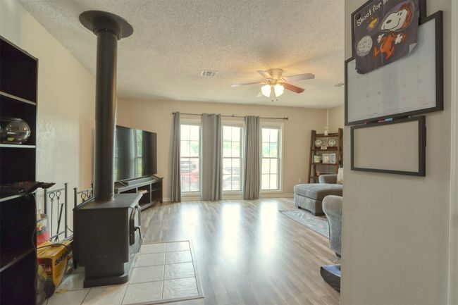 Living room with a wood stove, ceiling fan, a textured ceiling, and wood finished floors | Image 22