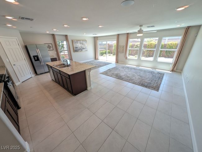 Kitchen with stainless steel refrigerator with ice dispenser, open floor plan, a ceiling fan, an island with sink, and light tile patterned flooring | Image 5