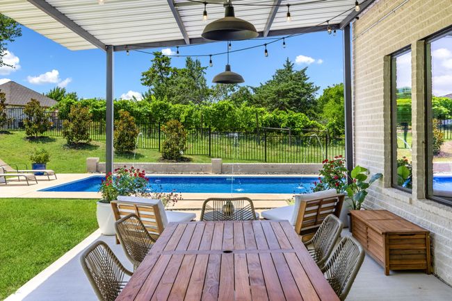 Fenced backyard with outdoor dining area and a covered patio area overlooking the sparkling pool. | Image 30