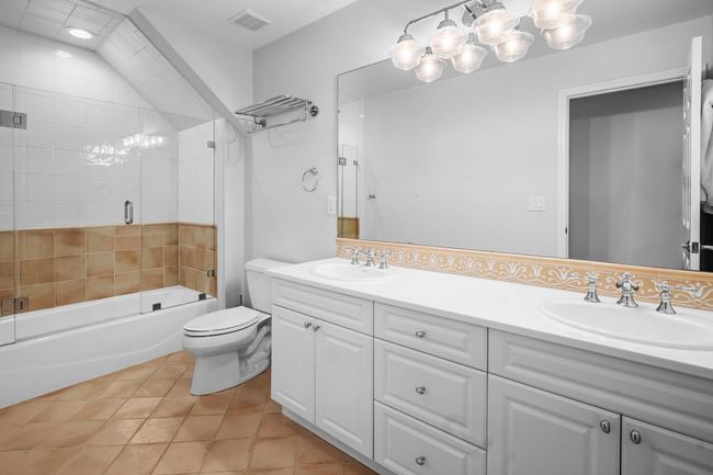 This full hall bath features a dual-sink vanity, glass-enclosed tub and shower combo, and charming tile accents—perfectly situated to serve additional bedrooms with both style and function. | Image 30