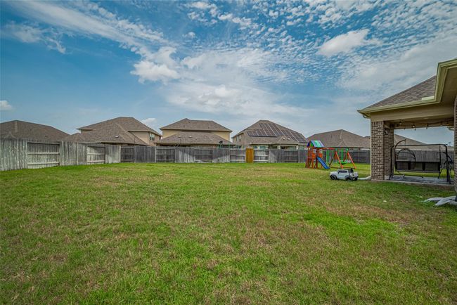 Spacious fenced backyard with a playset, patio area, and ample grass for activities, perfect for families. | Image 48