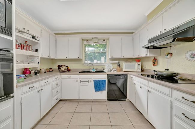 Kitchen with black appliances, under cabinet range hood, a sink, white cabinets, and light tile patterned flooring | Image 14