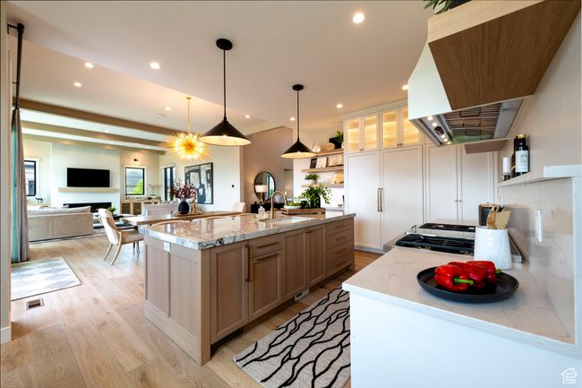 Kitchen featuring open shelves, wall chimney range hood, light wood-style floors, an island with sink, and light stone counters | Image 24