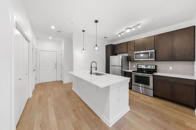 Kitchen featuring light wood finished floors, dark brown cabinets, stainless steel appliances, and a sink | Image 4