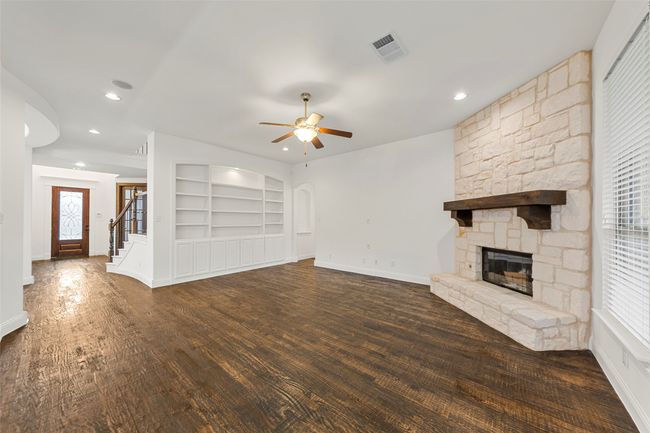 Unfurnished living room with visible vents, a fireplace, ceiling fan, built in shelves, and a wealth of natural light | Image 13