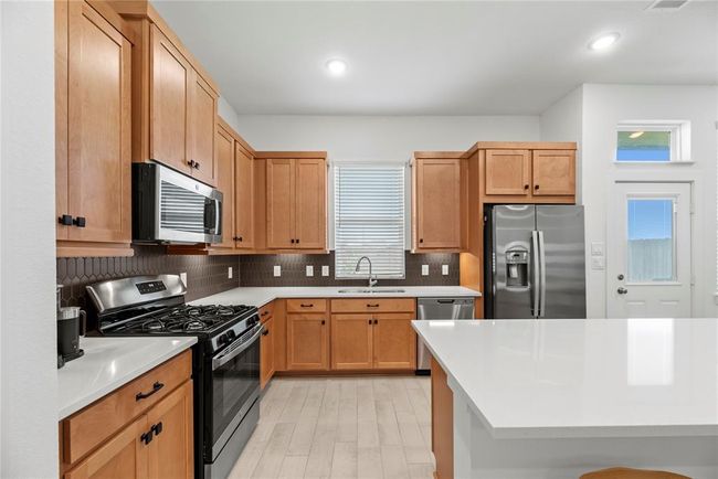 Beautiful cabinetry, under cabinet lighting, tile backsplash, Quartz countertops, stainless steel appliances, gas range and window above the sink with backyard views. | Image 10