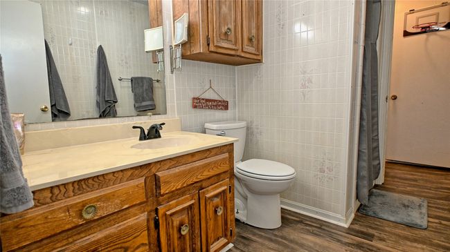 Full bathroom featuring a shower with curtain, toilet, tile walls, wood finished floors, and vanity | Image 9