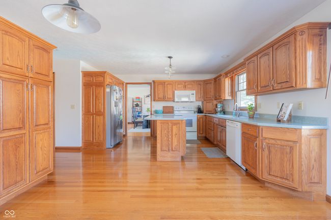 kitchen with light wood-type flooring, light countertops, a center island, and white appliances | Image 12