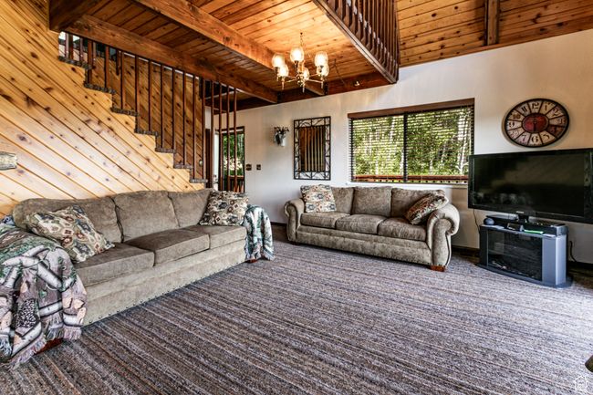 Living area featuring a wood ceiling with exposed beams, a chandelier, stairs, and carpet flooring | Image 6