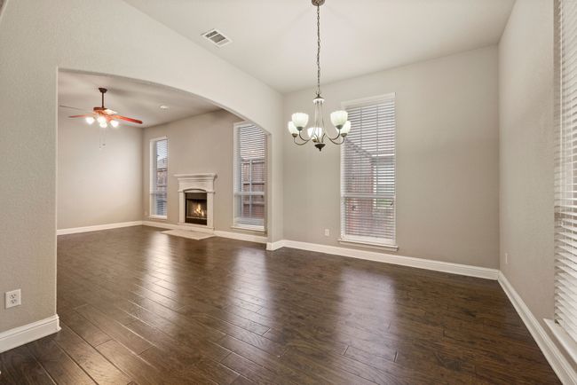Unfurnished living room with dark wood-style flooring, baseboards, visible vents, ceiling fan with notable chandelier, and a lit fireplace | Image 5