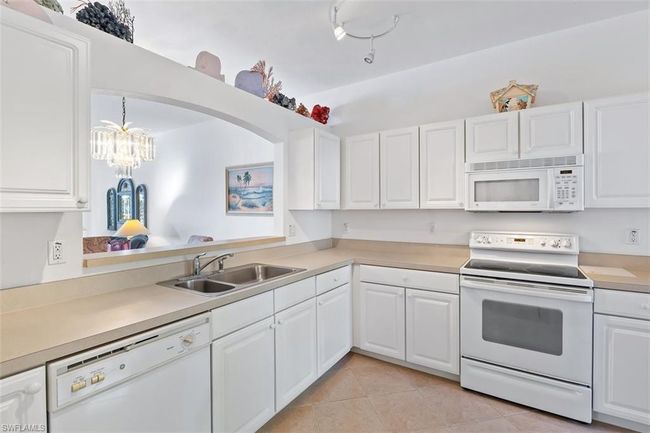 Kitchen with a chandelier, white cabinetry, sink, white appliances, and light tile floors | Image 12