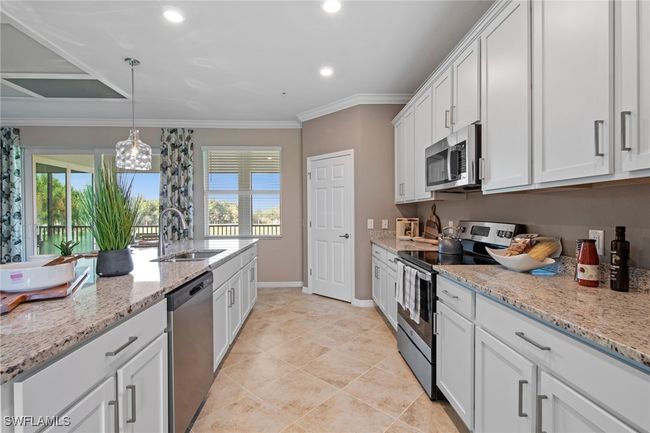 Kitchen with a sink, ornamental molding, white cabinetry, light stone countertops, and stainless steel appliances | Image 17