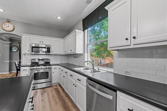Kitchen featuring stainless steel appliances, a sink, dark countertops, backsplash, and white cabinets | Image 15