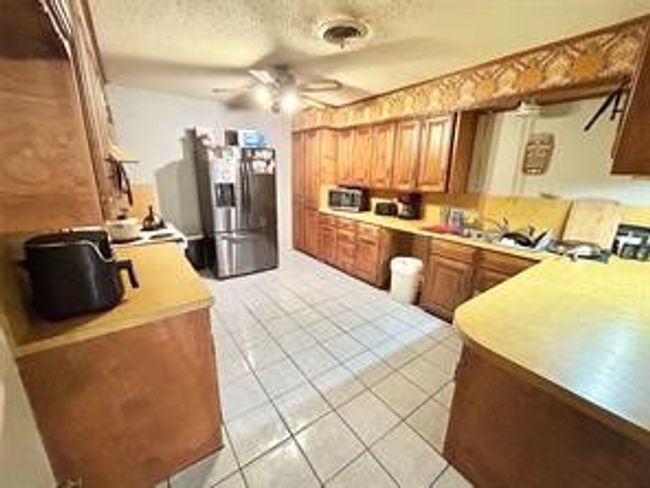 Kitchen featuring ceiling fan, light tile patterned floors, a textured ceiling, light countertops, and stainless steel fridge | Image 8
