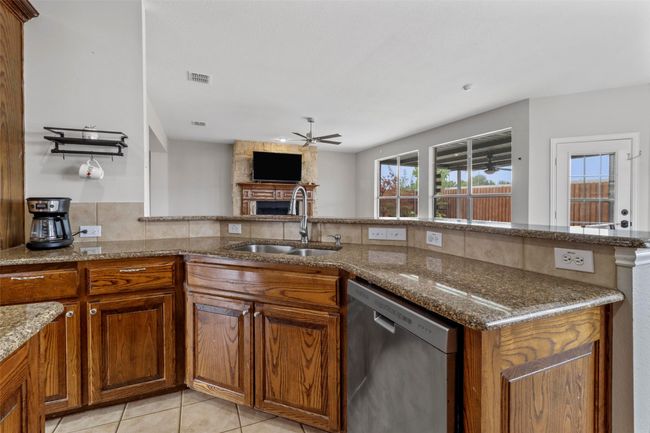 Kitchen with dishwasher, ceiling fan, brown cabinets, light tile patterned floors, and stone counters | Image 10