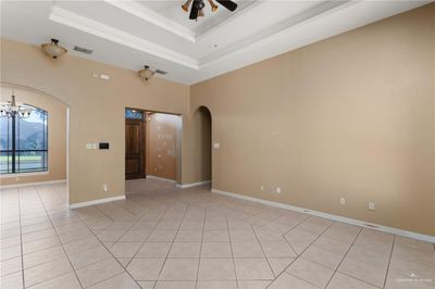 Tiled empty room featuring ceiling fan with notable chandelier and a raised ceiling | Image 2