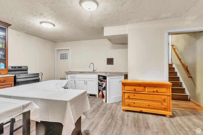 Kitchen with stainless steel electric range oven, a textured ceiling, light wood-style flooring, white cabinetry, and glass insert cabinets | Image 21