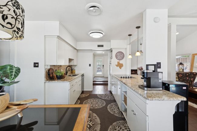 Kitchen featuring white cabinets, light stone countertops, hanging light fixtures, tasteful backsplash, and dark tile patterned floors | Image 6