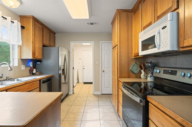 Kitchen featuring stainless steel appliances, a sink, light tile patterned flooring, brown cabinets, and decorative backsplash | Image 20