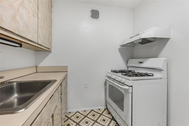 Kitchen featuring visible vents, baseboards, white gas stove, a sink, and under cabinet range hood | Image 7